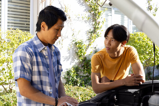 Fixing car engine, Asian father and teenage son discussing repairs in outdoor setting