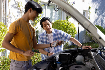 Checking car engine, Asian father and teenage son using smartphone for maintenance guidance
