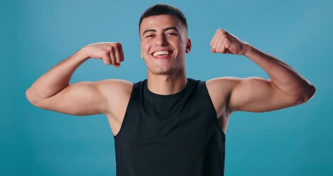 Face, flexing arms and man with pride, fitness and happiness on blue studio background. Portrait, person and model with bicep, strength or wellness with bodybuilder or workout with results or power