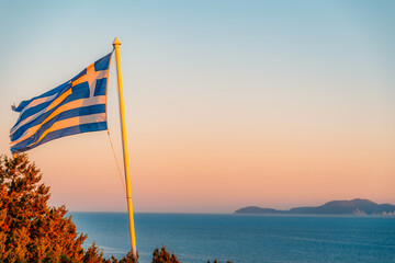 The national flag of Greece with a beautiful view of the sea  at sunrise near Lighthouse on Lefkada island, Greece.