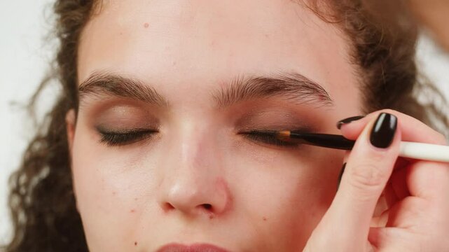 Eye shadow makeup to the upper eyelid, close-up. Makeup artist applies a bright eye shadow with a make-up brush.Tutorial master class of professional makeup, smoky eyes 