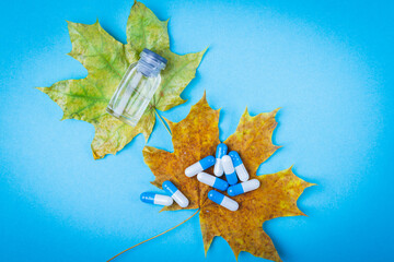 Tablets on autumn leaf. Autumn maple leaf and medicines on blue background.