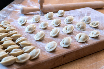 The raw dumplings were placed on a wooden cooking board. Next to it is a rolling pin for rolling out the dough and a tool for cutting the dough. Modeling dumplings by hand.
