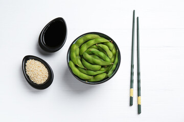 Fresh edamame pods, soy sauce and seeds on white wooden table, flat lay