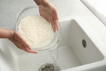 Woman rinsing rice in bowl above sink, closeup