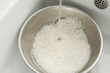 Pouring water into bowl with rice in sink, closeup