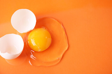Broken raw egg and shell on orange background, top view. Space for text