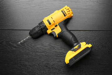 Cordless electric drill on black wooden table, top view