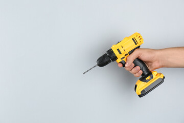 Fototapeta premium Man with cordless electric drill on light grey background, closeup. Space for text