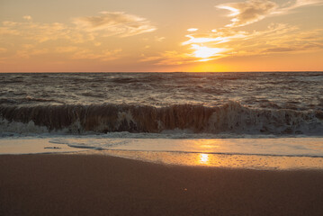 Obraz premium Sunset at sea during a storm. Coast with waves in sea on sunset. Waves in sea during storm and wind. Wave from the sea goes on land to the beach. Splashing Waves, Seaside.