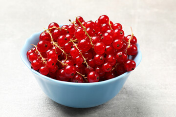 Fresh red currants in bowl on light grey table, closeup