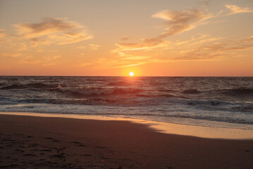 Fototapeta premium Sunset at sea during a storm. Coast with waves in sea on sunset. Waves in sea during storm and wind. Wave from the sea goes on land to the beach. Splashing Waves, Seaside.