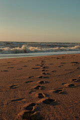 Sunset at sea during a storm. Coast with waves in sea on sunset. Waves in sea during storm and wind. Wave from the sea goes on land to the beach. sandy beach, footprints in the sand