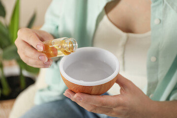 Woman adding essential oil to aroma diffuser at home, closeup