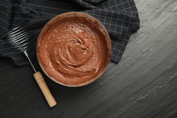 Chocolate dough in bowl and whisk on dark textured table, flat lay. Space for text