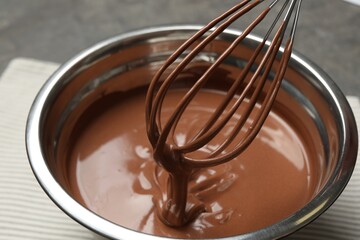 Chocolate dough dripping from whisk into bowl on table, closeup