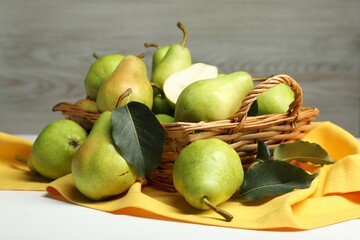 Fresh green pears with leaves and basket on white table, closeup