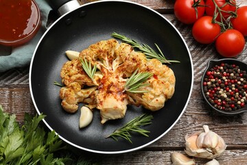 Tasty cauliflower steak in frying pan and other products on wooden table, top view