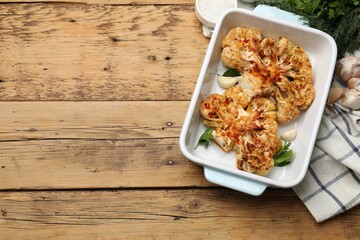 Tasty cauliflower steaks in baking dish and spices on wooden table, top view. Space for text