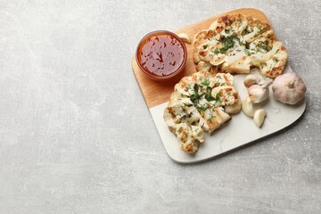 Delicious grilled cauliflower steaks with sauce and garlic on grey table, above view. Space for text