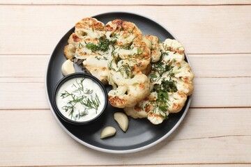 Delicious grilled cauliflower steaks with sauce, garlic and dill on wooden table, top view