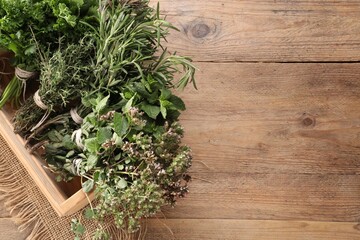Bunches of different aromatic herbs in crate on wooden table, above view. Space for text
