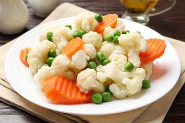 Tasty cooked cauliflower with green peas and carrot slices on white wooden table, closeup