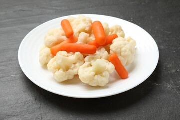Tasty cauliflower with baby carrots on black table, closeup