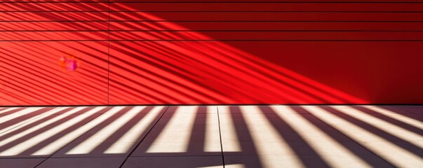 Dynamic red wall with horizontal lines and dramatic shadows casting textured patterns in sunlight, creating a modern and abstract architectural composition
