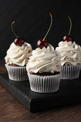 Delicious cupcakes with cream and cherries on wooden table, closeup