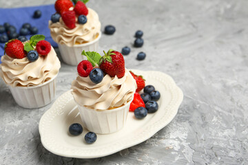 Tasty cupcakes with different berries and mint on light grey table, space for text