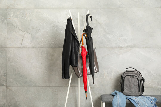 Colorful umbrellas, jacket and bag on clothing rack near gray marble wall