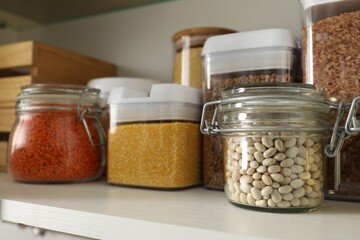 Different types of cereals and legumes in containers on shelf