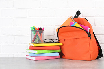 Backpack with different school stationery on light grey table near brick wall