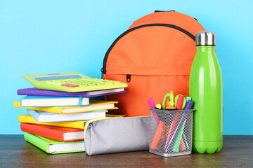 Backpack with different school stationery on wooden table against light blue background
