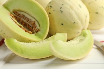 Fresh whole and cut honeydew melons on white wooden table, closeup