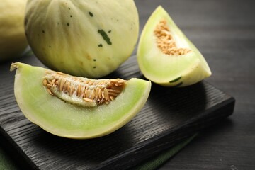 Fresh whole and cut honeydew melons on black wooden table, closeup