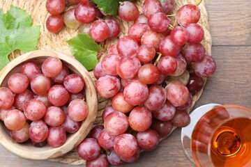 Obraz premium Fresh ripe grapes and glass of wine on wooden table, flat lay