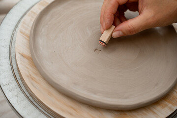 Decorating clay products with special patters and symbols on a ceramics workshop. Using a clay stamp to engrave letters and ornaments on a pottery project.