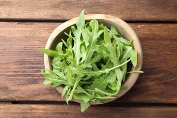 Fresh green arugula leaves in bowl on wooden table, top view