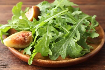 Fresh green arugula leaves and cut fig on wooden table, closeup