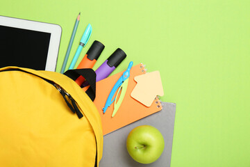 Backpack, different school stationery and apple on light green background, flat lay. Space for text