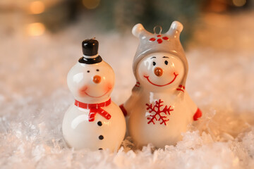Funny snowman figures on artificial snow against blurred background, closeup