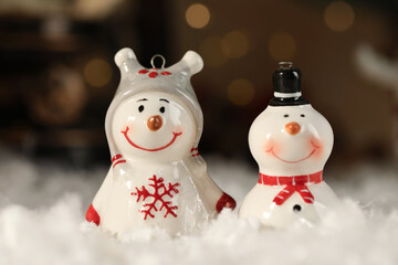 Funny snowman figures on artificial snow against blurred lights, closeup