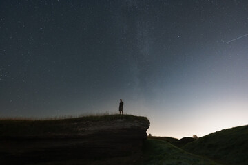 Fototapeta premium Night scene, a man with a night vision device stands on a cliff. The starry sky and the milky way.