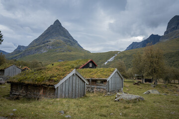 Old wooden huts with green grass on roof in front of landmark mountain in Norway