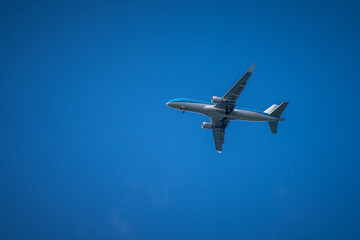 Blue and white airplane flying bottom view with blue sky in background