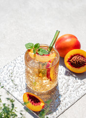 Peach lemonade with ice and mint on a concrete background. Fresh iced tea in a glass with shadow and fruits.