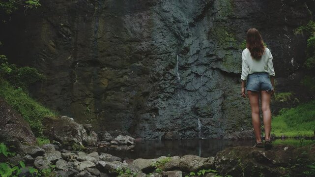 Young woman enjoying a peaceful waterfall in a lush forest, surrounded by greenery and tranquility. Experience nature's beauty in french polynesia