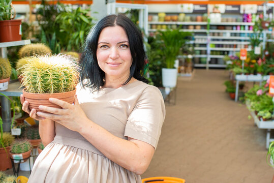 41 year old pregnant woman holding a pot with a large cactus in a flower shop. shopping during pregnancy, pregnancy after 40.